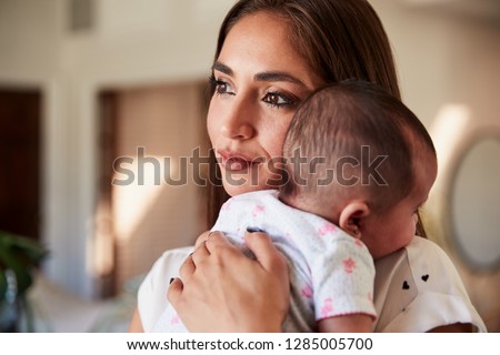Millennial Hispanic mother holding her newborn son close to her chest, head and shoulders, close up
