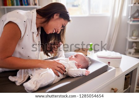 Happy mother changing the diaper of her baby at home on a changing table, waist up, close up