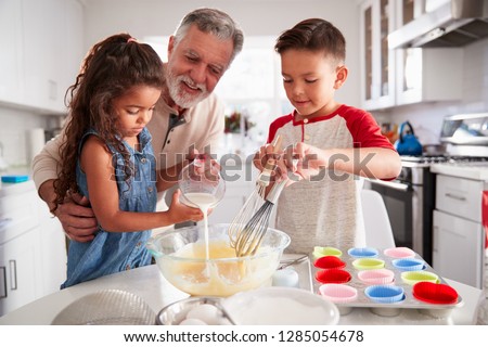 Brother and sister standing at the kitchen table making cake mix with their grandfather, close up