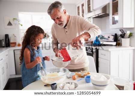 Young girl preparing cake mixture with her grandfather at the kitchen table, close up