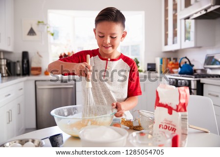 Pre-teen boy making a cake in the kitchen mixing cake mix, smiling, close up