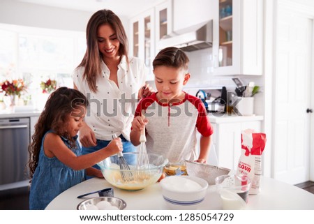 Brother and sister making cake mixture together at the kitchen table with their mum, waist up