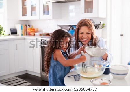Young Hispanic girl making cake in the kitchen with her grandma, looking down