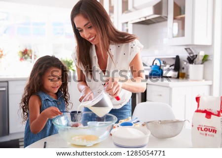Young Hispanic girl making cake in the kitchen with help from her mum, waist up