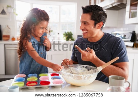 Young girl stands at the kitchen table making cakes with her father, tasting the cake mix, close up