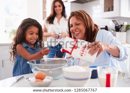 Young girl making a cake in the kitchen with her grandmother, mum stands watching, selective focus