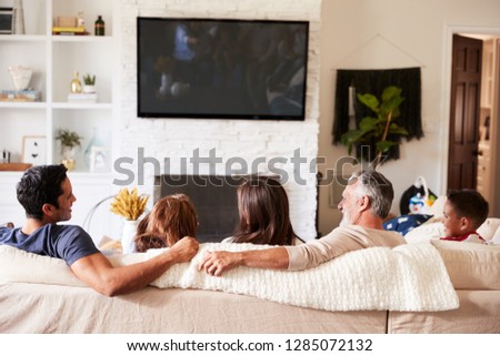 Back view of three generation Hispanic family on the sofa watching TV, grandad looking at adult son