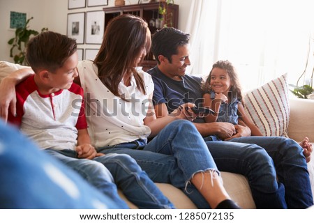 Young Hispanic family sitting on the sofa at home to watch TV, looking at each other, close up