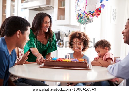 Close up of African American three generation family sitting together at the kitchen table celebrating the pre-teen daughters birthday with a birthday cake