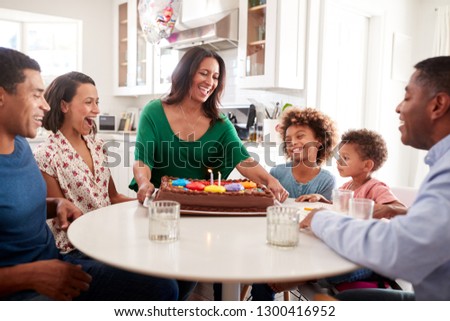 Excited three generation African American family sitting together in the kitchen celebrating a birthday, grandmother bringing the cake to the table