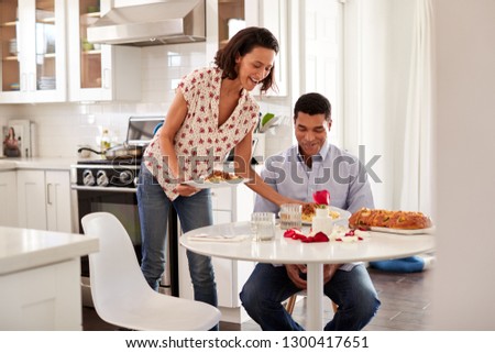 Young African American adult man sitting at the table in the kitchen is served a romantic meal by his partner, selective focus