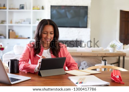 Smiling African American middle aged woman sitting at a table drawing on a tablet computer with a stylus, front view