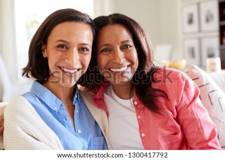 Close up of young African American adult woman sitting on the sofa in living room with her mother smiling to camera, close up