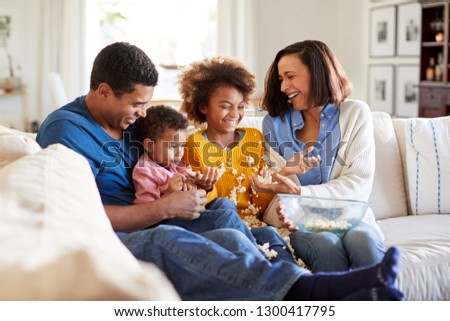 Young African American family sitting together on the sofa in their living room watching a scary movie, clearing up spilled popcorn, selective focus