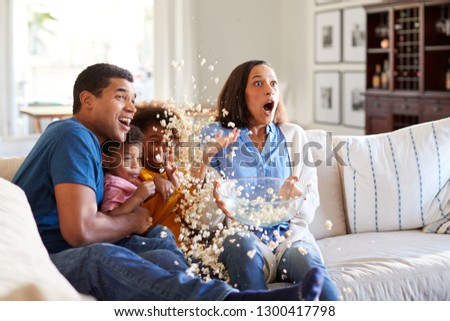 Young African American family sitting together on the sofa in their living room watching a scary movie accidentally throwing popcorn in the air