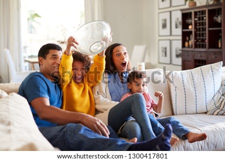 Young African American family sitting together on the sofa in their living room watching a scary movie