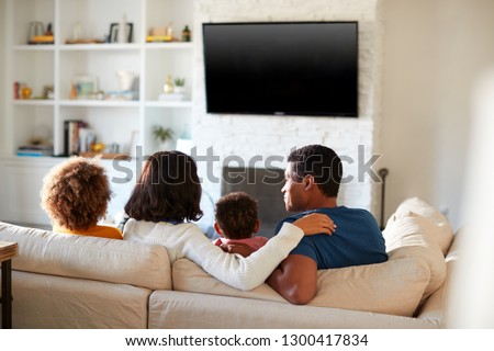 Back view of African American young family sitting on the sofa and watching TV together in their living room, close up