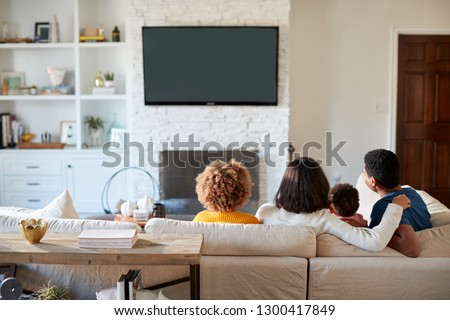 Back view of young African American family sitting on the sofa and watching TV together in their living room