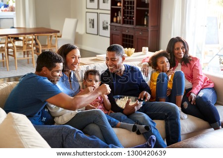 Three generation African American family   sitting on the sofa in living room, watching TV and eating popcorn together, elevated view