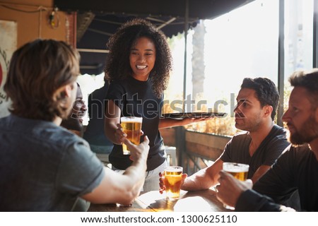 Waitress Serving Drinks To Group Of Male Friends Meeting In Sports Bar