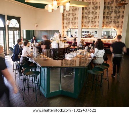 Interior Of Busy Cocktail Bar In Restaurant With Staff Serving Customers