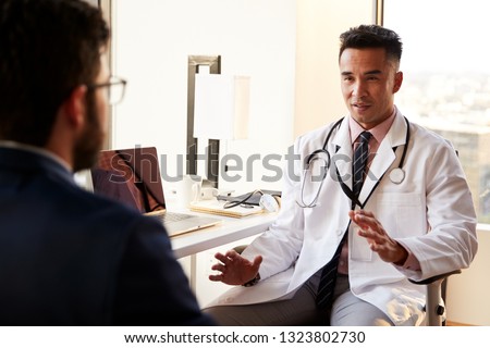 Over The Shoulder View Of Man Having Consultation With Male Doctor In Hospital Office