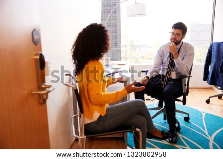 Woman Having Consultation With Male Doctor Viewed Through Door Of Hospital Office