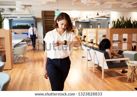 Businesswoman Walking Through Modern Office Checking Health Data On Smart Watch