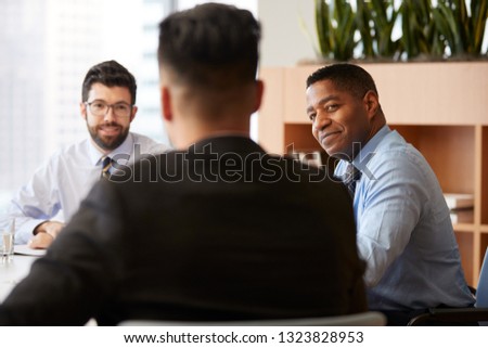 Three Businessmen Sitting Around Table Meeting In Modern Open Plan Office