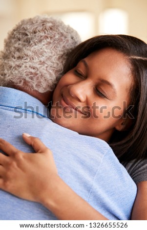 Over The Shoulder View Of Senior Father Being Hugged By Adult Daughter At Home