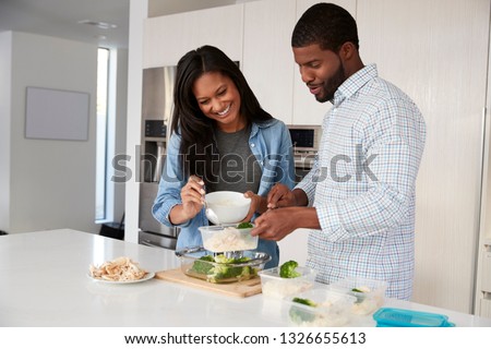 Couple In Kitchen Preparing High Protein Meal And Putting Portions Into Plastic Containers