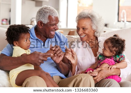Grandparents Sitting On Sofa At Home Playing With Baby Granddaughters