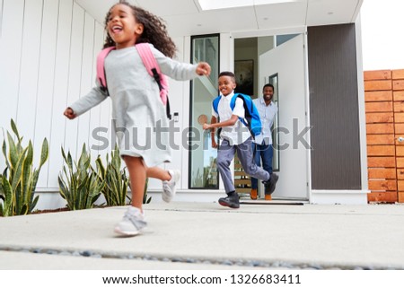 Excited Children Running Out Of Front Door On Way To School Watched By Father
