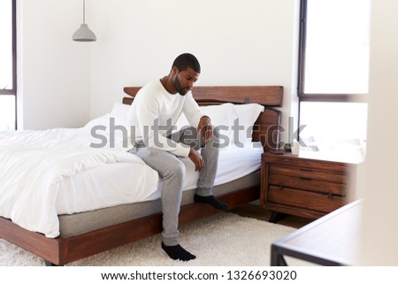 Depressed Man Looking Unhappy Sitting On Side Of Bed At Home