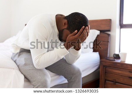 Depressed Man Looking Unhappy Sitting On Side Of Bed At Home With Head In Hands