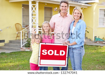 Family Standing By Sold Sign Outside Home