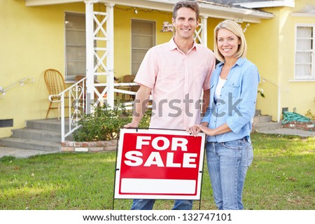 Couple Standing By For Sale Sign Outside Home