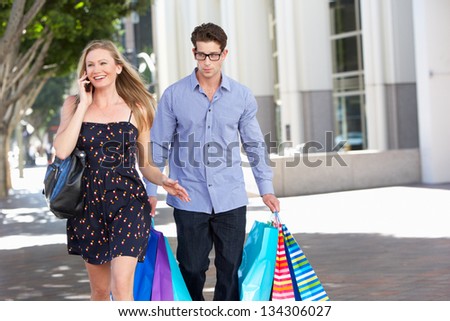 Fed Up Man Carrying Partners Shopping Bags On City Street