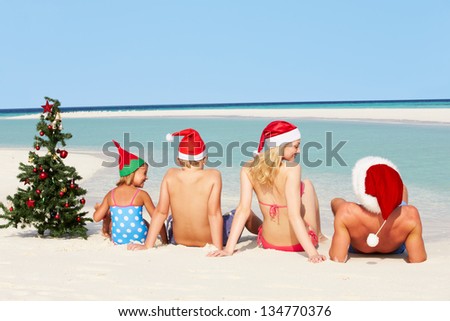 Family Sitting On Beach With Christmas Tree And Hats