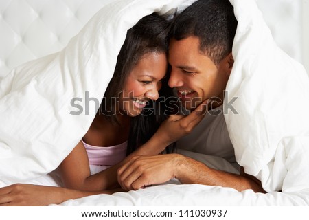 Couple Relaxing In Bed Hiding Under Duvet