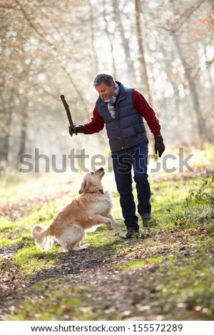 Man Throwing Stick For Dog On Walk Through Autumn Woods