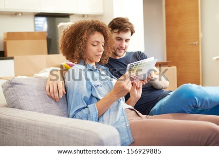 Couple Sitting On Sofa Looking At Paint Charts
