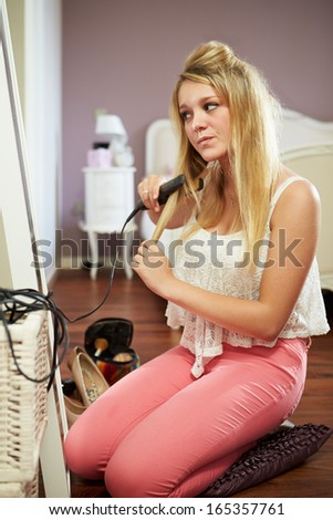 Teenage Girl Straightening Hair In Bedroom