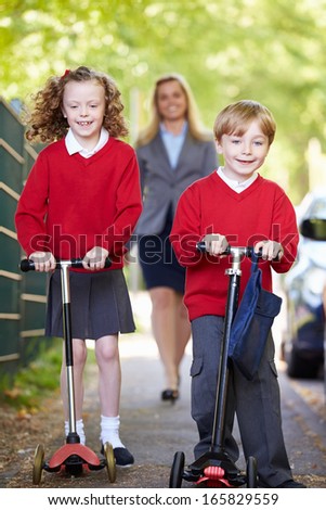 Children Riding Scooters On Their Way To School With Mother