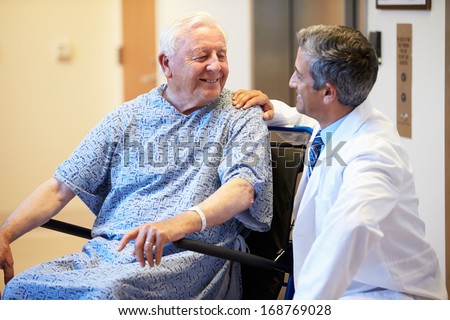 Senior Male Patient Being Pushed In Wheelchair By Doctor