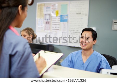 Male And Female Nurse In Discussion At Nurses Station
