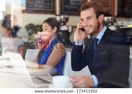Businessman Using Mobile Phone And Laptop In Coffee Shop