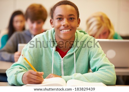 Male High School Student Studying At Desk In Classroom