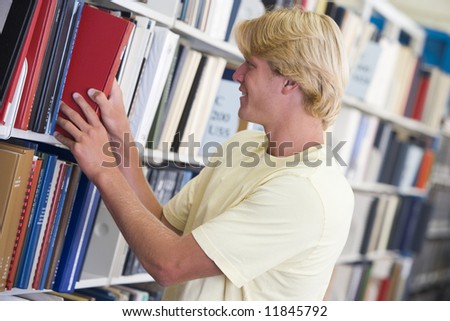 Male university student selecting book from library shelf