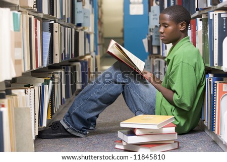 Male university student sitting on library floor surrounded by books